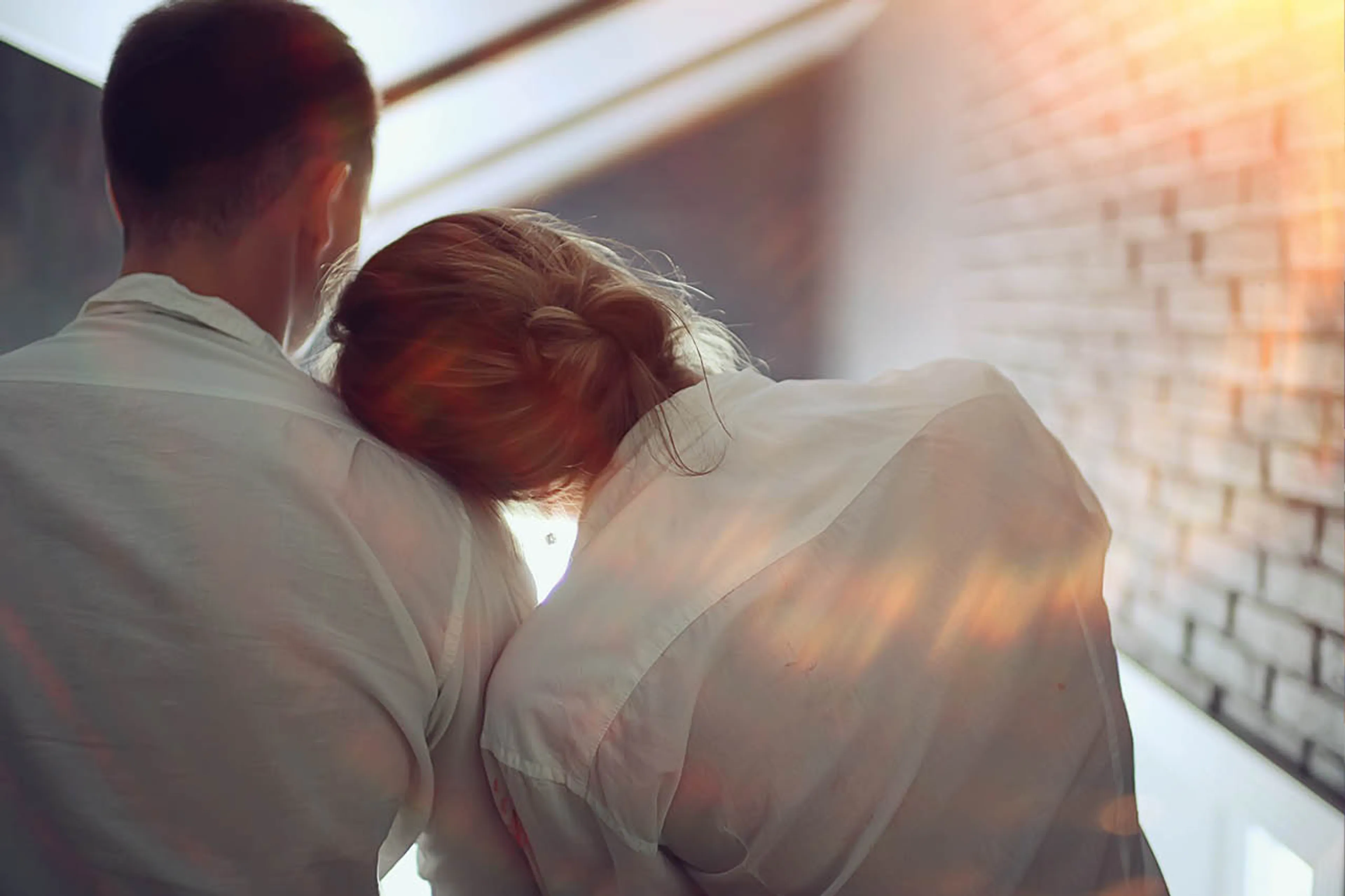 Man en vrouw van de achterkant. Vrouw leunt met hoofd op schouder van de man.